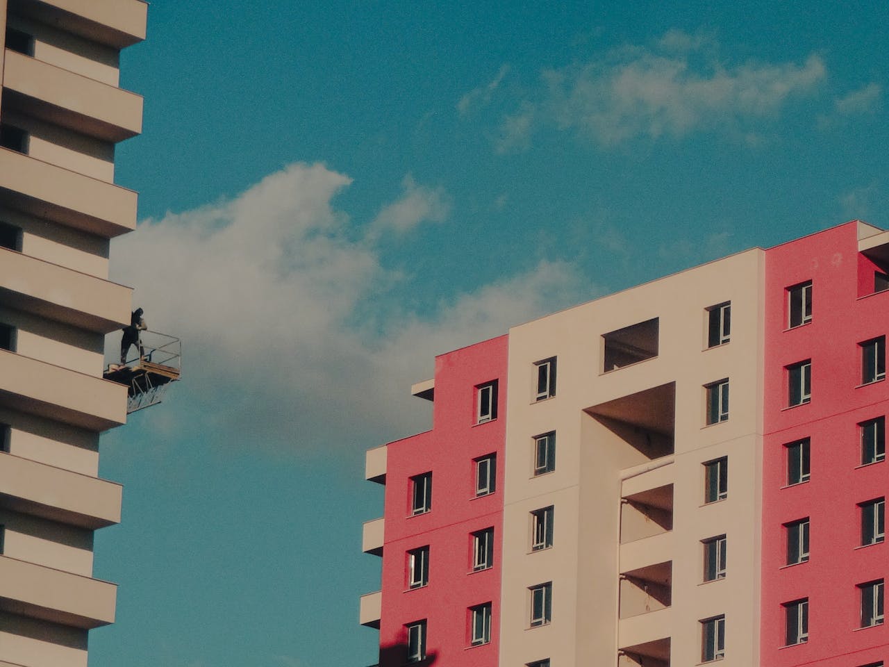 hero-img-02 Colorful high-rise buildings with a worker on a suspended platform against a clear sky.