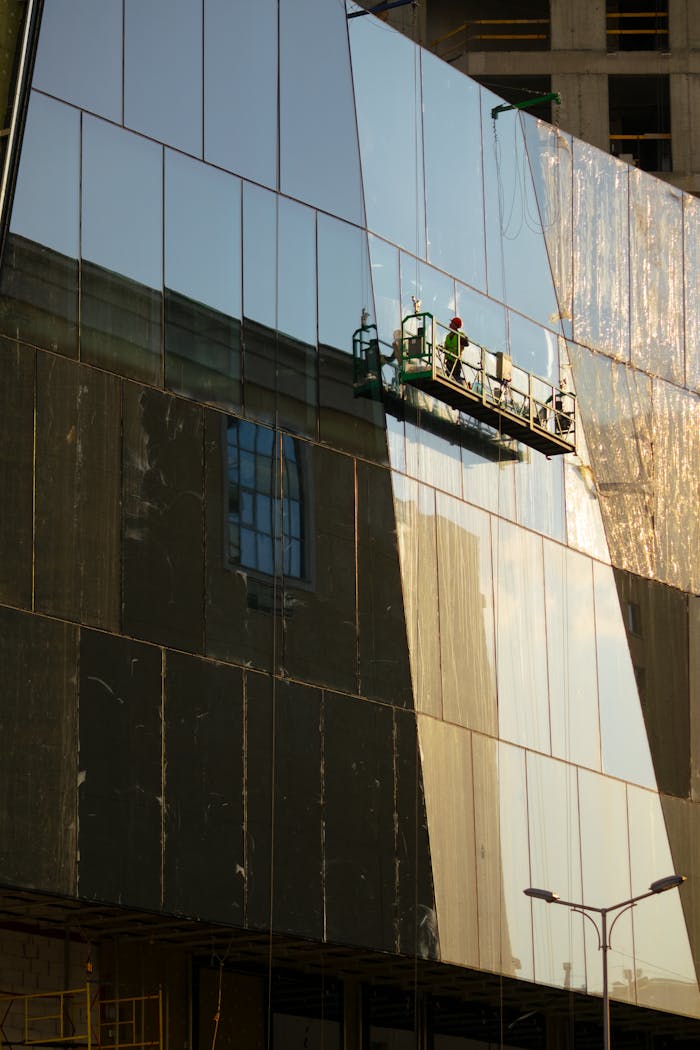 services-03 A worker on a lift cleans the glass facade of a modern skyscraper in daylight.