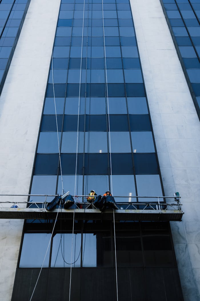 services-01 Professionals cleaning a skyscraper's windows from a suspended platform high above the ground.